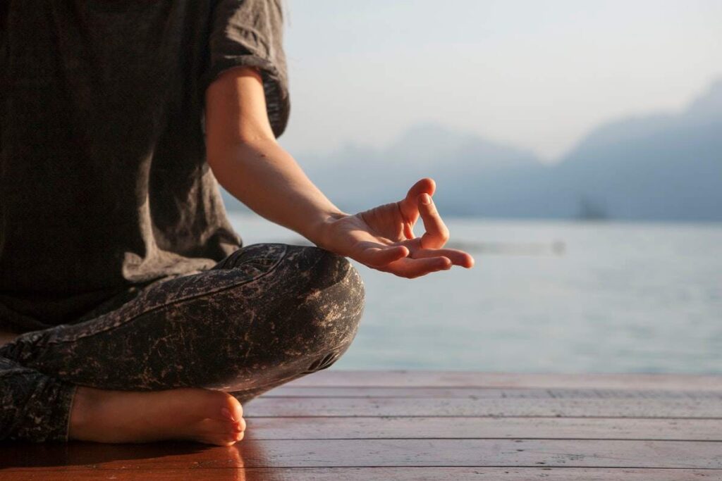 Woman sitting cross legged on yoga mat near window practicing deep breathing