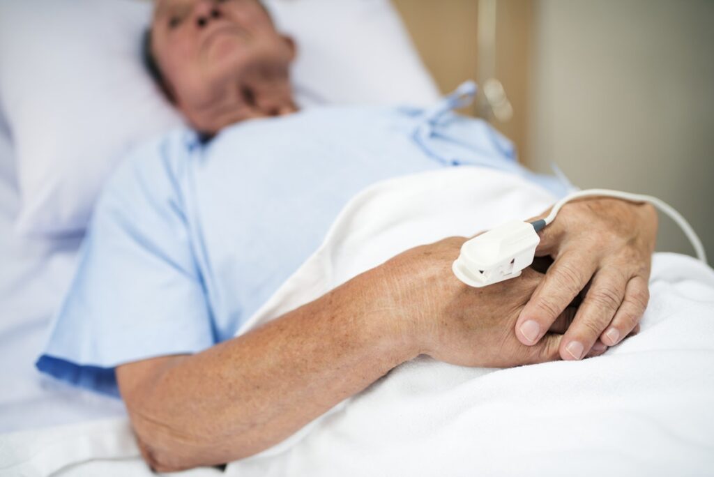 Man lying in hospital bed holding his stomach with a pained expression