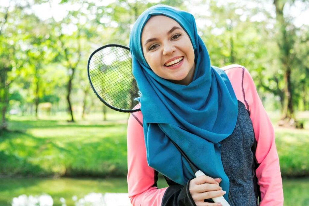 Smiling woman in hijab holding tennis racket outdoors