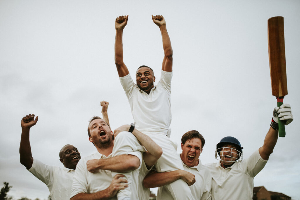Group of happy cricketer raising arms outdoors celebrating success