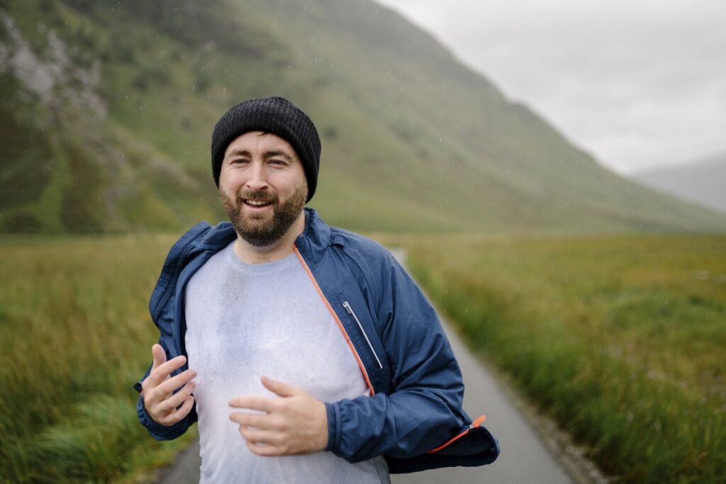 Man wearing hoodie holding water bottle and smiling after outdoor workout