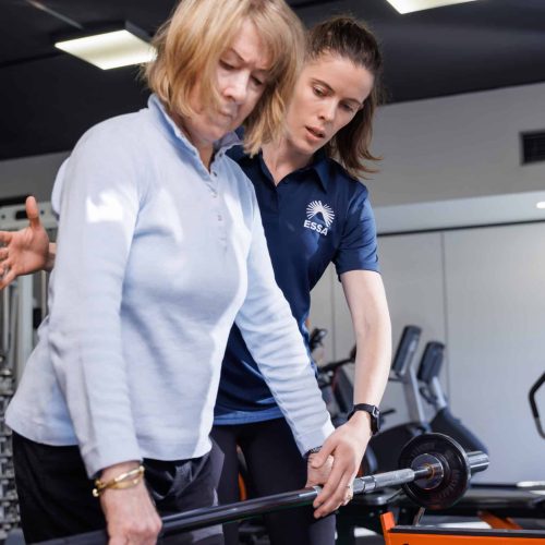 Trainer assisting older woman with weight training in gym